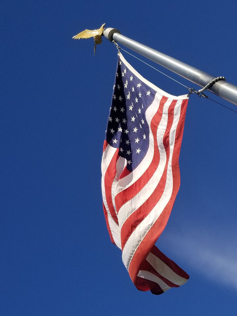 American flag waving against a clear blue sky, topped with an eagle emblem, symbolizing patriotic pride.