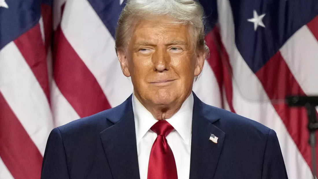 A man in a dark suit and red tie stands in front of American flags, smiling confidently, representing patriotism on Presidents’ Day.
