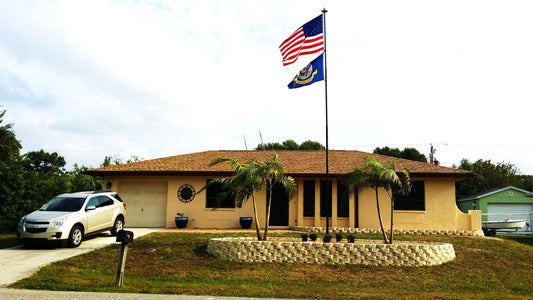 FLying two flags on a telescoping flagpole with a house and palm trees behind it in the landscaping 