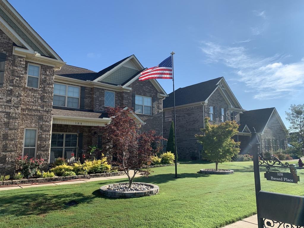 American flag flying proudly outside brick homes, showcasing spring greenery and a clear blue sky.