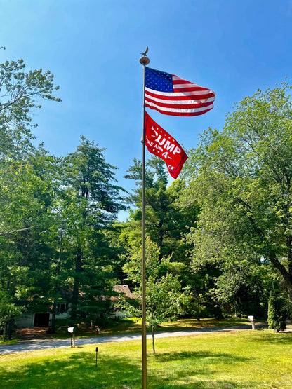 20-foot gold flagpole with American flag and red promotional banner, by Atlantic Flagpole, set in a green landscape.